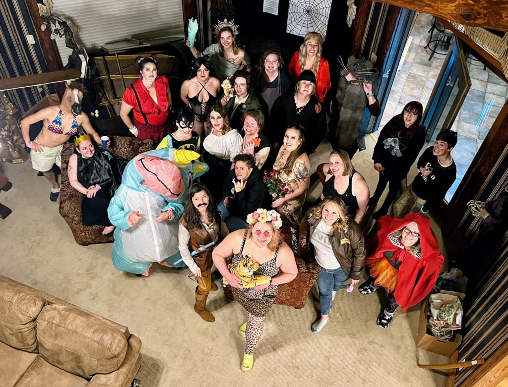 A group of people in costumes smiling, look up at the camera in a mountain lodge.